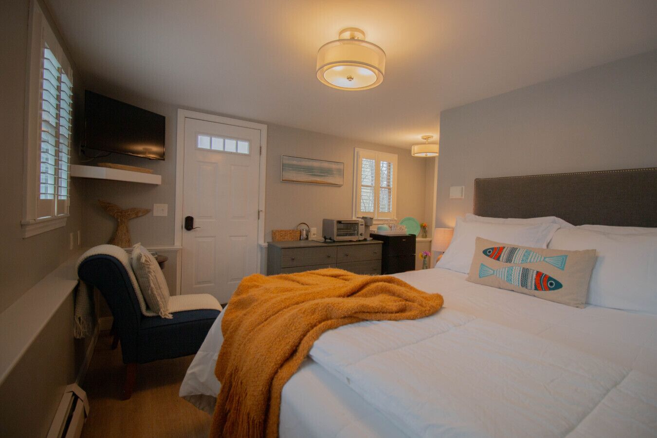 Un dormitorio con cama, una silla, escritorio, televisor y puerta.