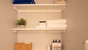 Ein Badezimmer mit Toilette, drei Ablagen mit Handtüchern, einer Pflanze, einem Korb und Toilettenartikeln.