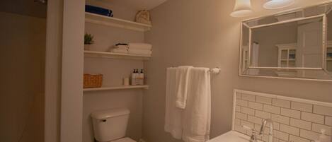 A bathroom with a toilet, a sink with a mirror, and shelves above the toilet.