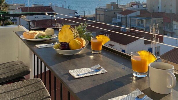 A balcony with a table set for breakfast, featuring a bowl of fruit, a glass of orange juice, and a mug. - Cozy apartment in Santa Pola with WiFi (Santa Pola)