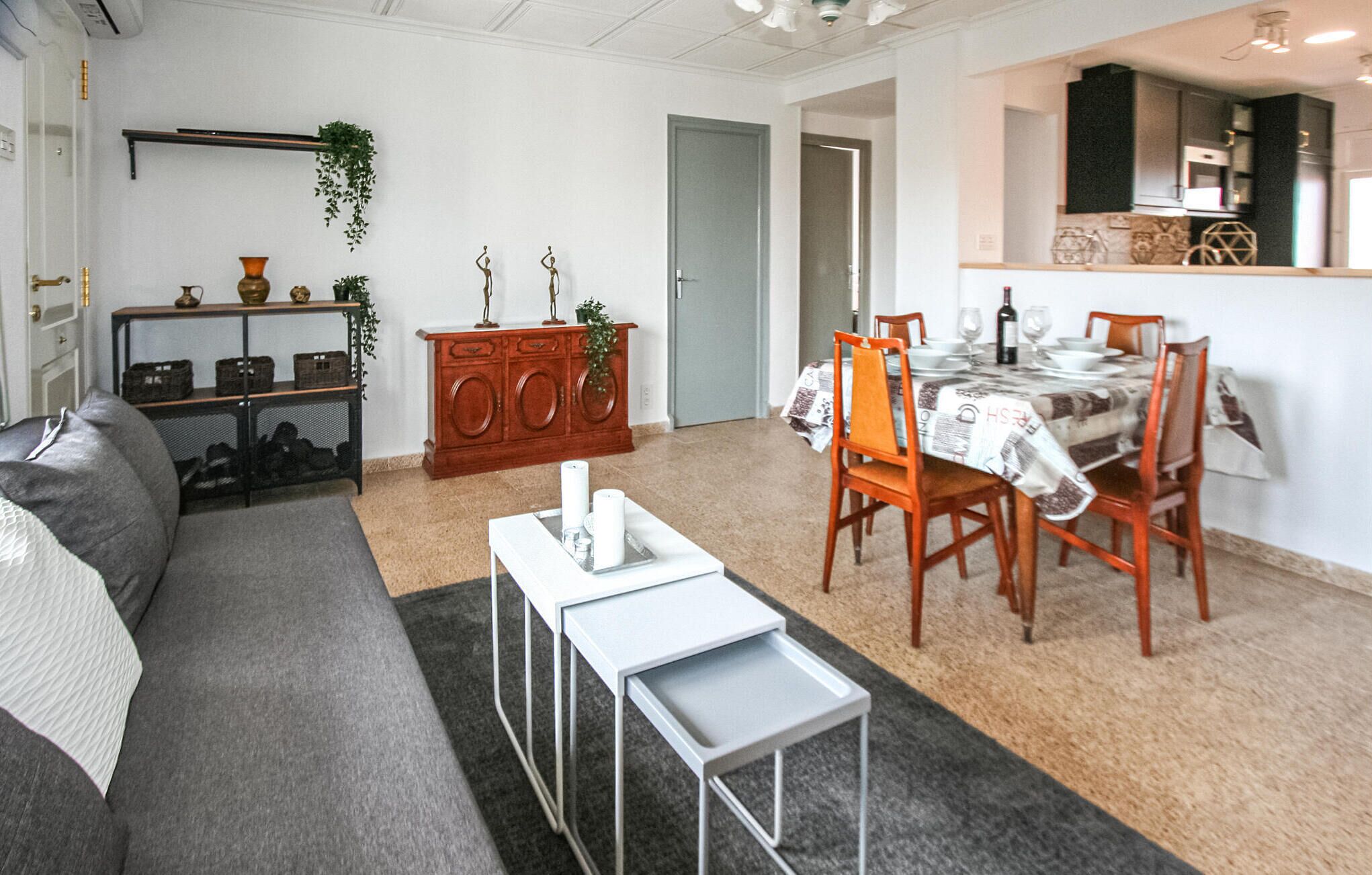 A living room with a grey sofa, a small white table, and a dining area with a table set for two.