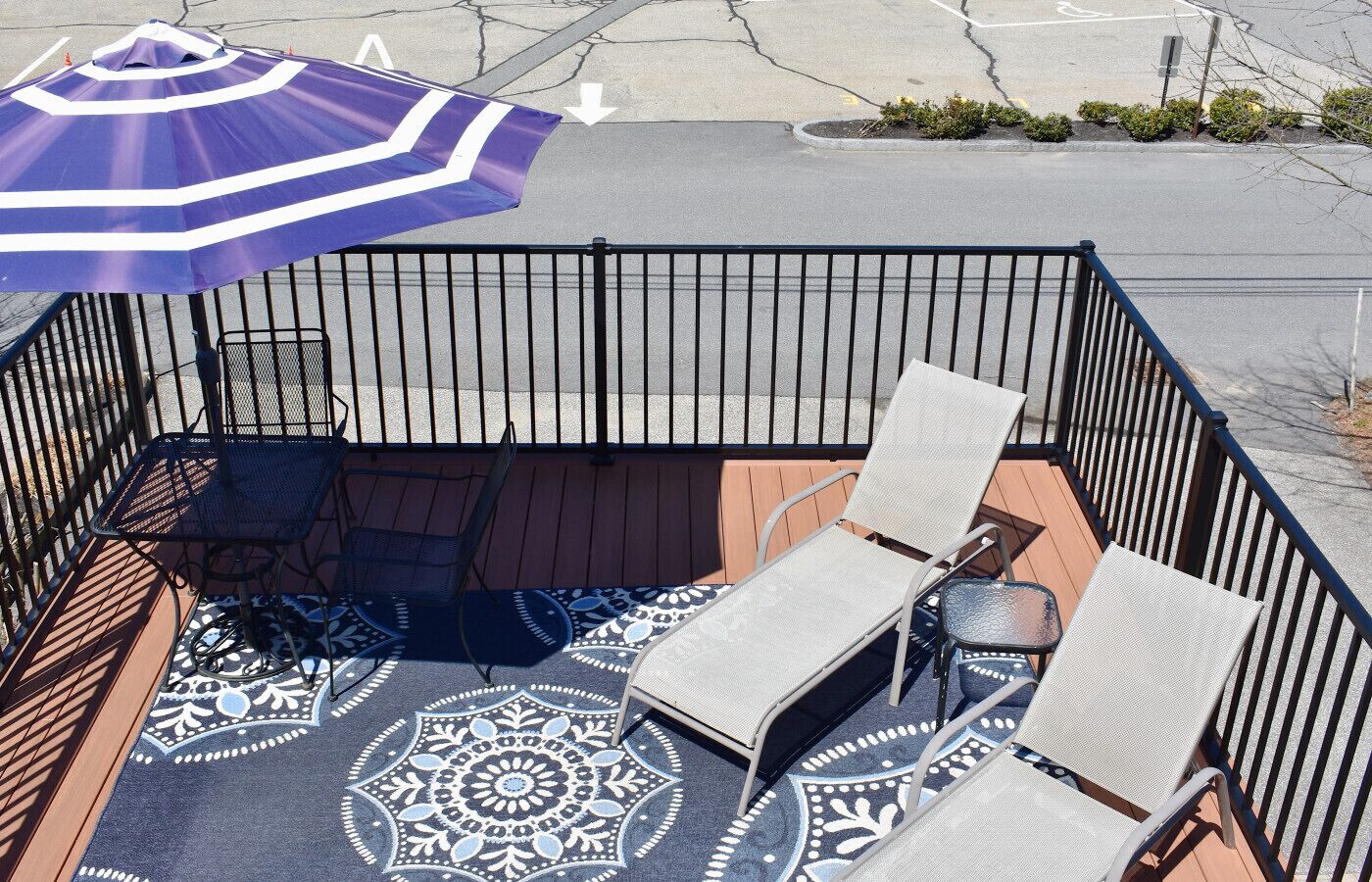 Uma área de pátio com tapete estampado, uma mesa, duas cadeiras e um guarda-sol.