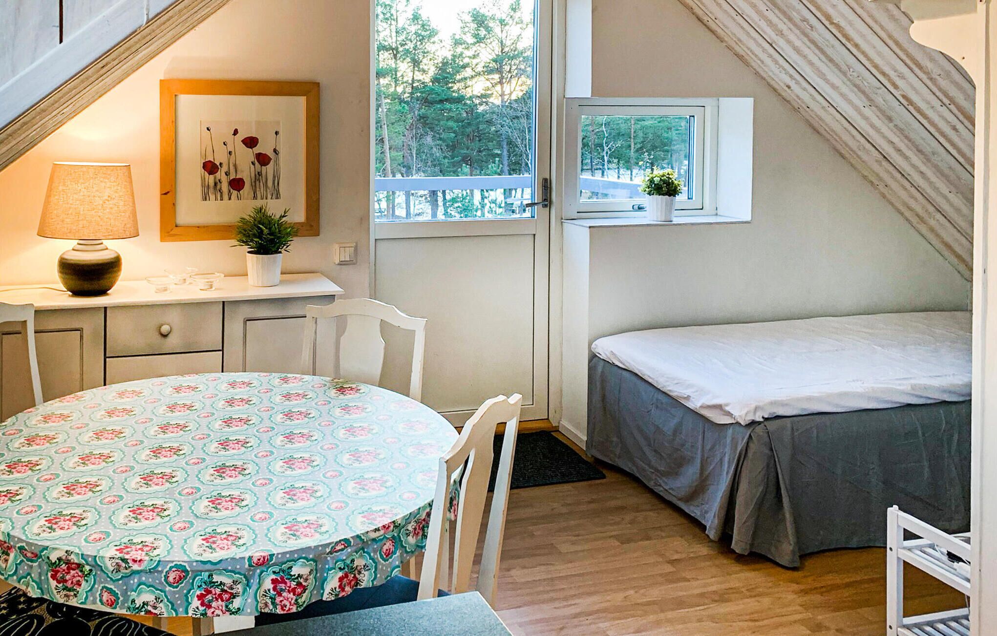 Een knus, klein kamertje met een ronde tafel, een bed en een raam met uitzicht op een bos.