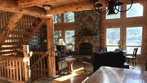 A rustic cabin interior with a stone fireplace, wooden beams, and a cozy seating area. - Rustic Mountain Cabin (New Meadows)