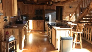 A rustic kitchen with wooden cabinets, a stainless steel refrigerator, and a wooden bar stool. - Rustic Mountain Cabin (New Meadows)
