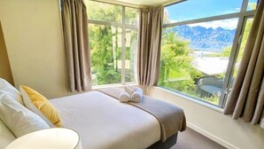 A bedroom with a large bed, a bedside table with a lamp, and a view of mountains through the window.
