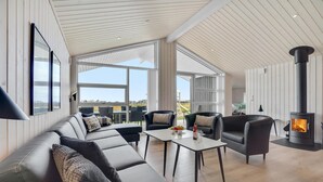 Ein modernes Wohnzimmer mit einer Couch, Sesseln, einem Tisch und einem Kaminofen.