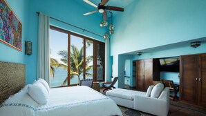 A room with a large bed, a sofa, a TV, and a view of the ocean.