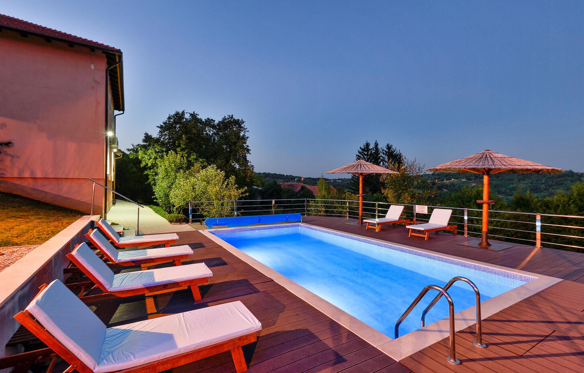 A swimming pool with lounge chairs and umbrellas, surrounded by a wooden deck and overlooking a scenic landscape.