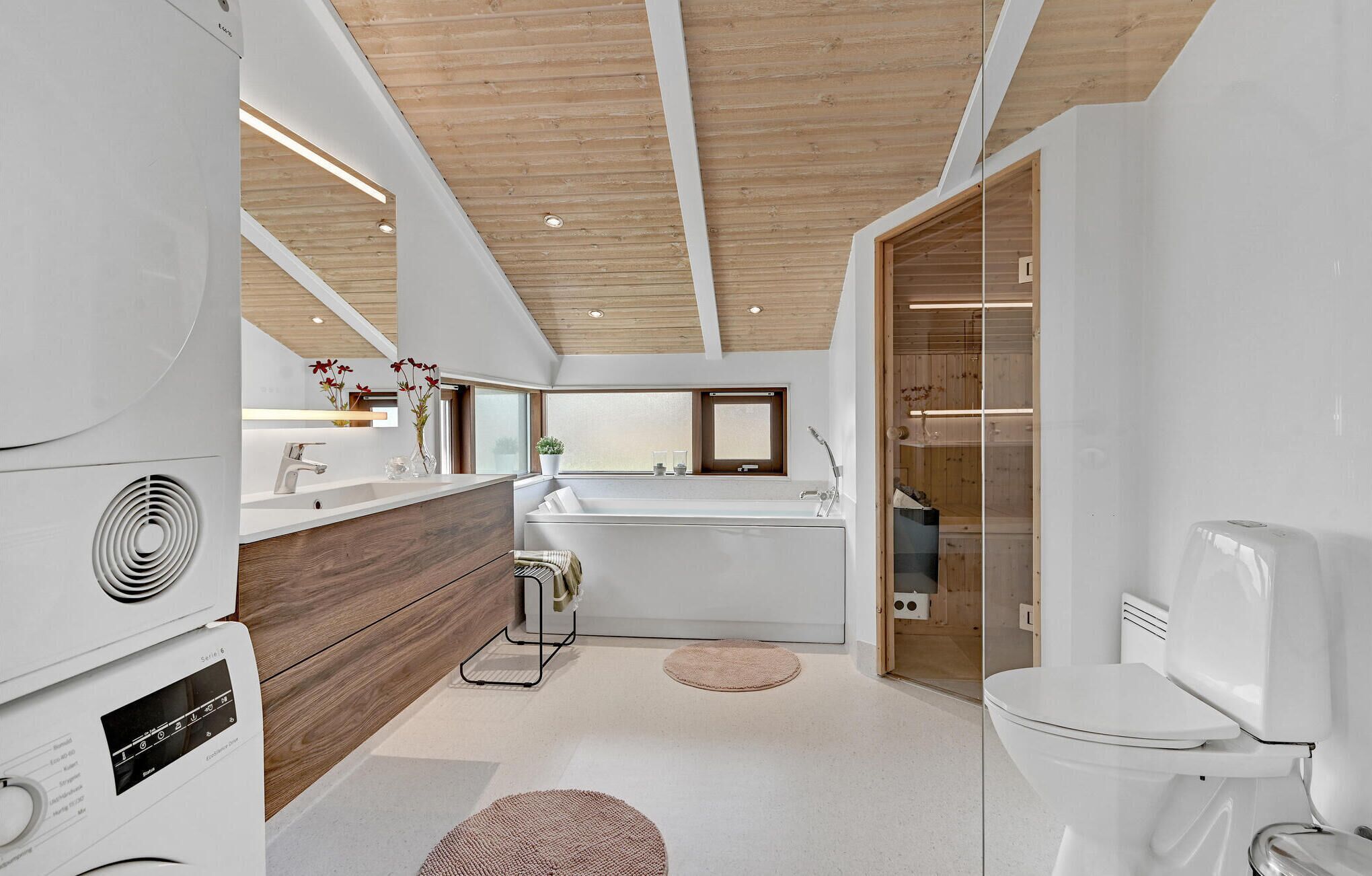 Ein modernes Badezimmer mit Holzboden, weißen Armaturen und einem großen Fenster.