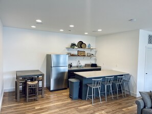 Eine moderne Küche mit einem Edelstahlkühlschrank, einem Holzespeisetisch mit Stühlen, einer Bar mit Hockern und einem Mülleimer.
