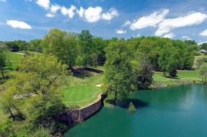 Ein Golfplatz mit einem Wasserabschnitt, umgeben von Bäumen und wolkenlosem Himmel.