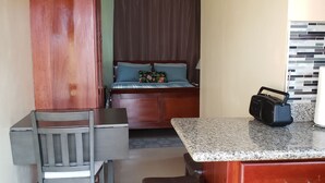 Une pièce de taille modeste comprenant un lit, un bureau, une chaise, une petite table et un coin cuisine.