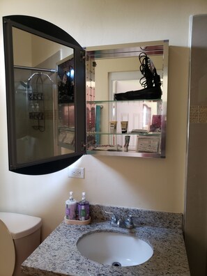Une salle de bain dotée d’un comptoir en granit, d’un lavabo blanc, d’un miroir et d’une cabine de douche.