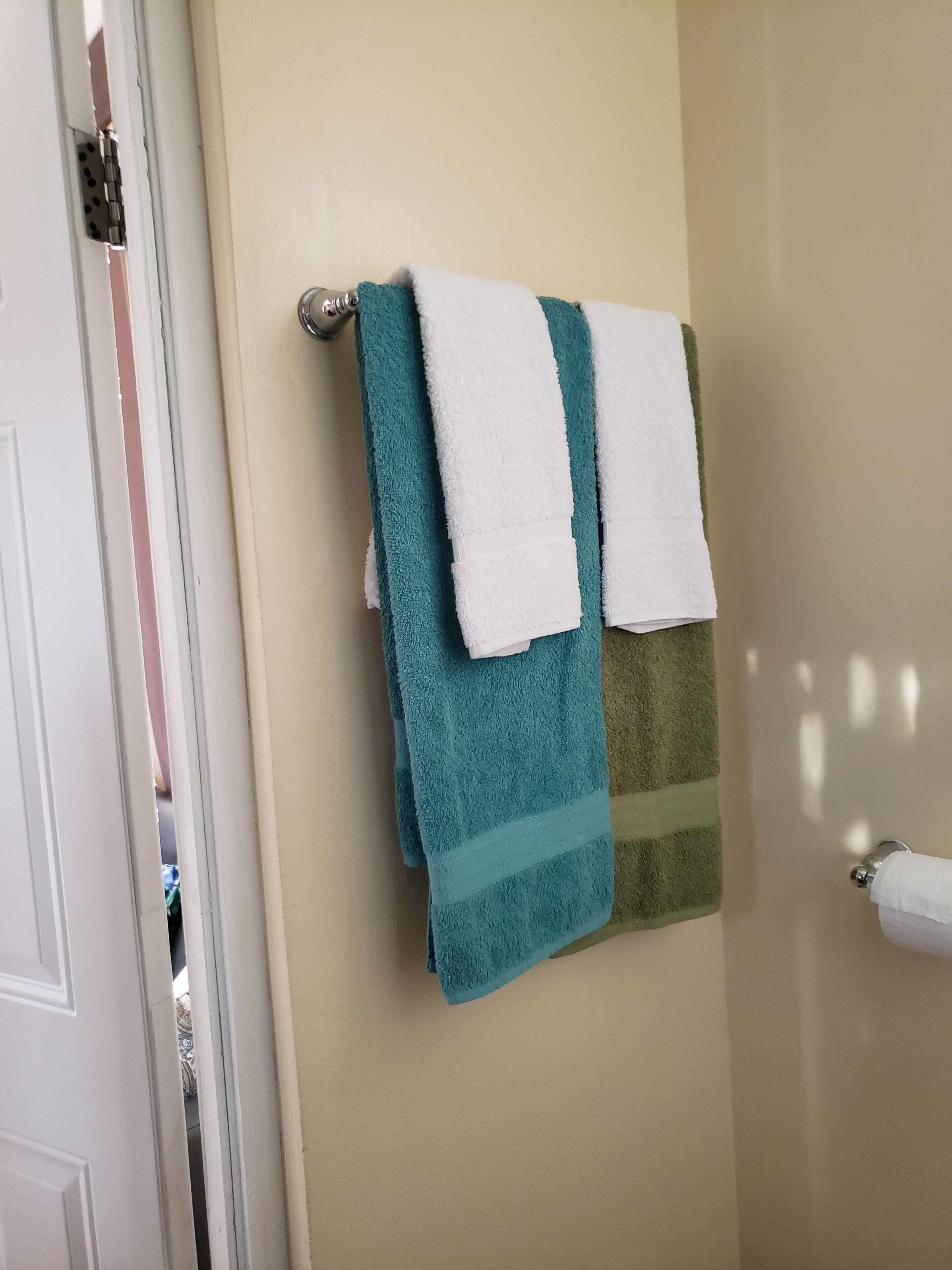A bathroom with a beige wall, a towel rack holding three towels, and a toilet paper holder.