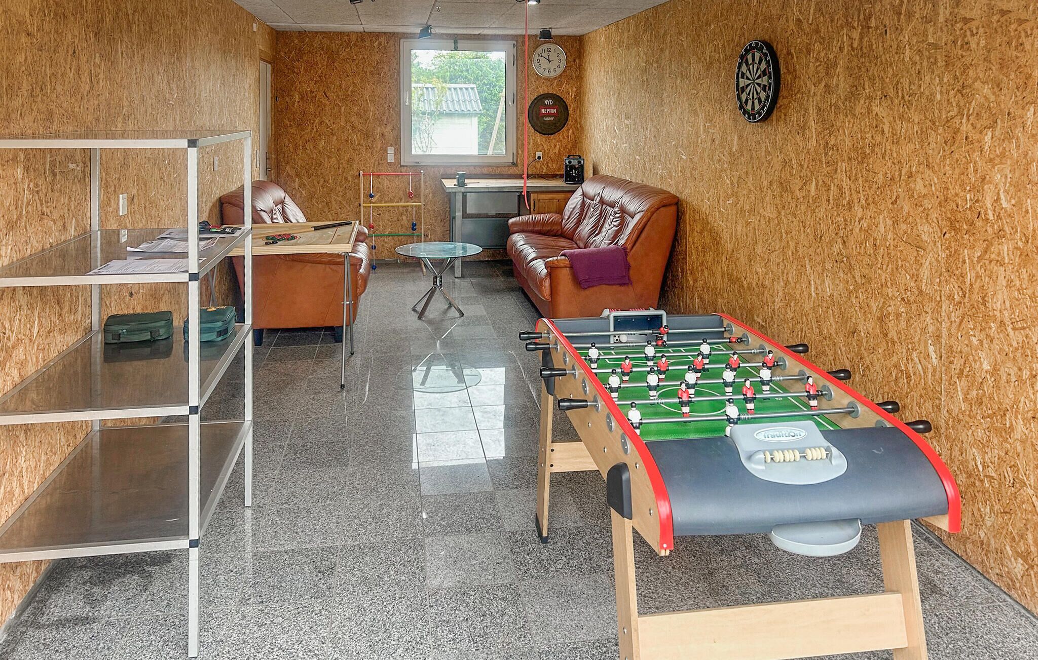 Ein Zimmer mit Kicker, einer Couch, einem Couchtisch und einer Dartscheibe.