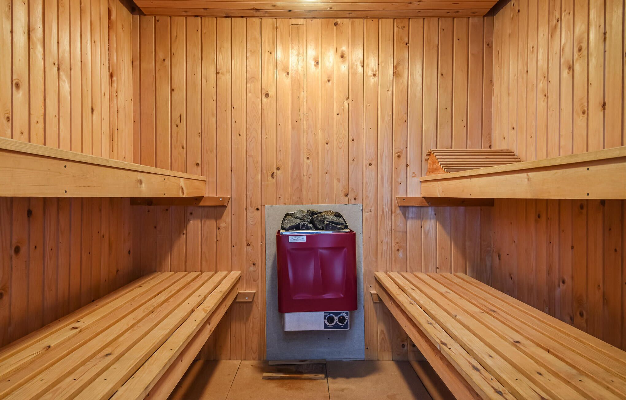 A sauna room with wooden benches and a red sauna heater.