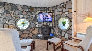 Ein gemütliches Zimmer mit Steinwänden, einem Kamin, einem Fernseher und bequemen Sitzgelegenheiten.