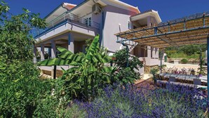 A two-story house with a balcony, surrounded by lush greenery and flowering plants. - 1 bedroom lovely apartment in Barbat na Rabu (Barbat na Rabu)