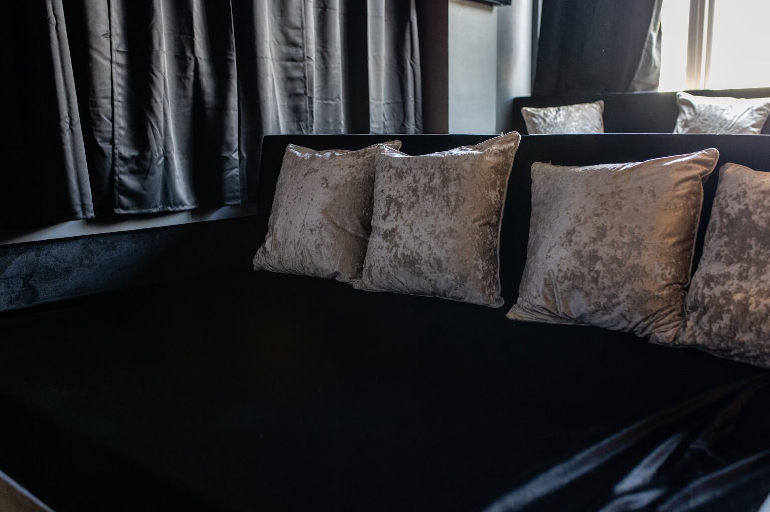 Een bed met een zwart hoofdeinde en vier grijze kussens.