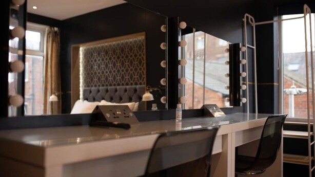 A modern hotel room with a vanity mirror, makeup essentials, and a comfortable bed. - Hollywood Suite Sasco Apartments (Blackpool)