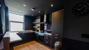 A modern kitchen with dark cabinetry, a wooden countertop, and a built-in oven. - Hollywood Suite Sasco Apartments (Blackpool)