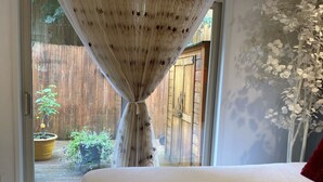 A bedroom with a large bed, a sliding glass door leading to a wooden deck, and a view of a garden. - FIFA WORLD CUP!!! Luxury Lakefront Lake Sammamish Apartment (Redmond)
