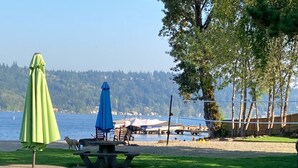 A grassy area with picnic tables and umbrellas, a body of water, and boats in the background. - FIFA WORLD CUP!!! Luxury Lakefront Lake Sammamish Apartment (Redmond)
