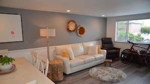 A living room with a white sofa, a dining table with chairs, a lamp, a bicycle, and a window with blinds. - FIFA WORLD CUP!!! Luxury Lakefront Lake Sammamish Apartment (Redmond)