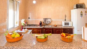 A kitchen with granite countertops, a stove, a microwave, and a refrigerator. There are three bowls of fruits and vegetables on the counter. - Beautiful home in Olivares (Olivares)