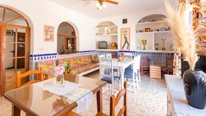 A dining area with a glass table, white chairs, a bench with colorful floral tiles, and a ceiling fan. - Beautiful home in Olivares (Olivares)