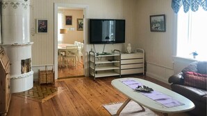 A living room with a wooden floor, a white sofa, a television, a dining area with a table and chairs, and a fireplace. - Gorgeous home in Rörvik with WiFi (Rörvik)