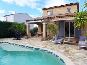 Un espace aménagé au bord de la piscine, avec une piscine carrelée, des sièges d’extérieur et une pergola.