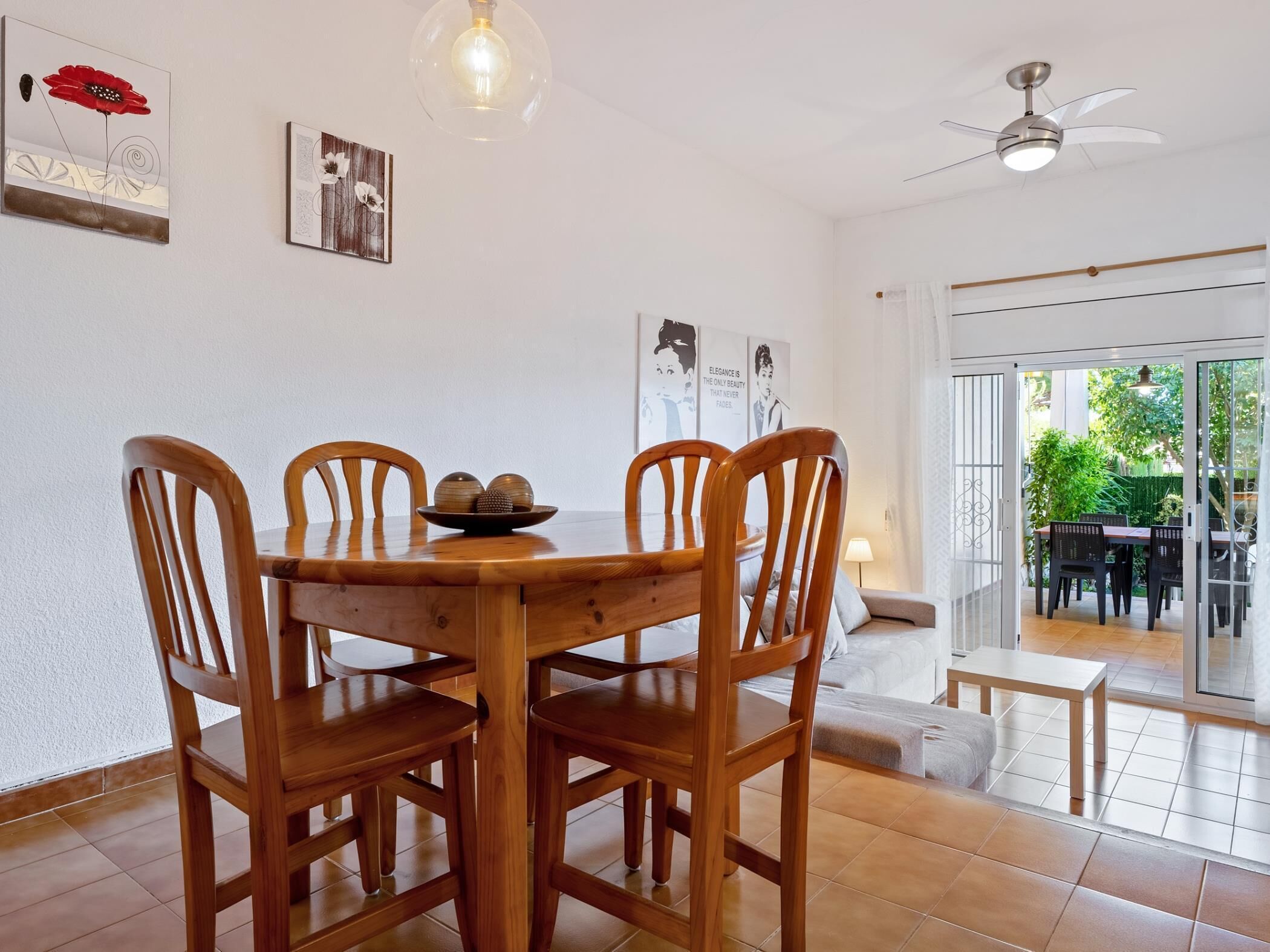 Un comedor con una mesa y sillas de madera, un ventilador de techo y vistas al exterior a través de un ventanal.