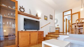 Ein Wohnzimmer mit Fernseher, Holzkredänzen, einem weißen Tisch und einer Treppe, die in einen anderen Raum führt.