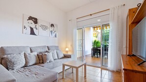 Ein modernes Wohnzimmer mit einem grauen Sofa, einem kleinen Tisch und einem Fernseher auf einem Holzgestell.