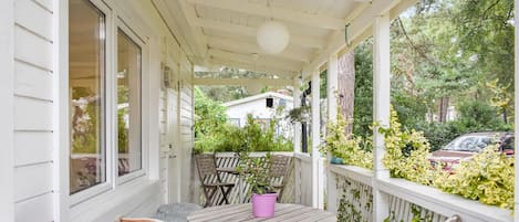 A covered porch with a table and chairs, a potted plant, and a view of a house and trees.