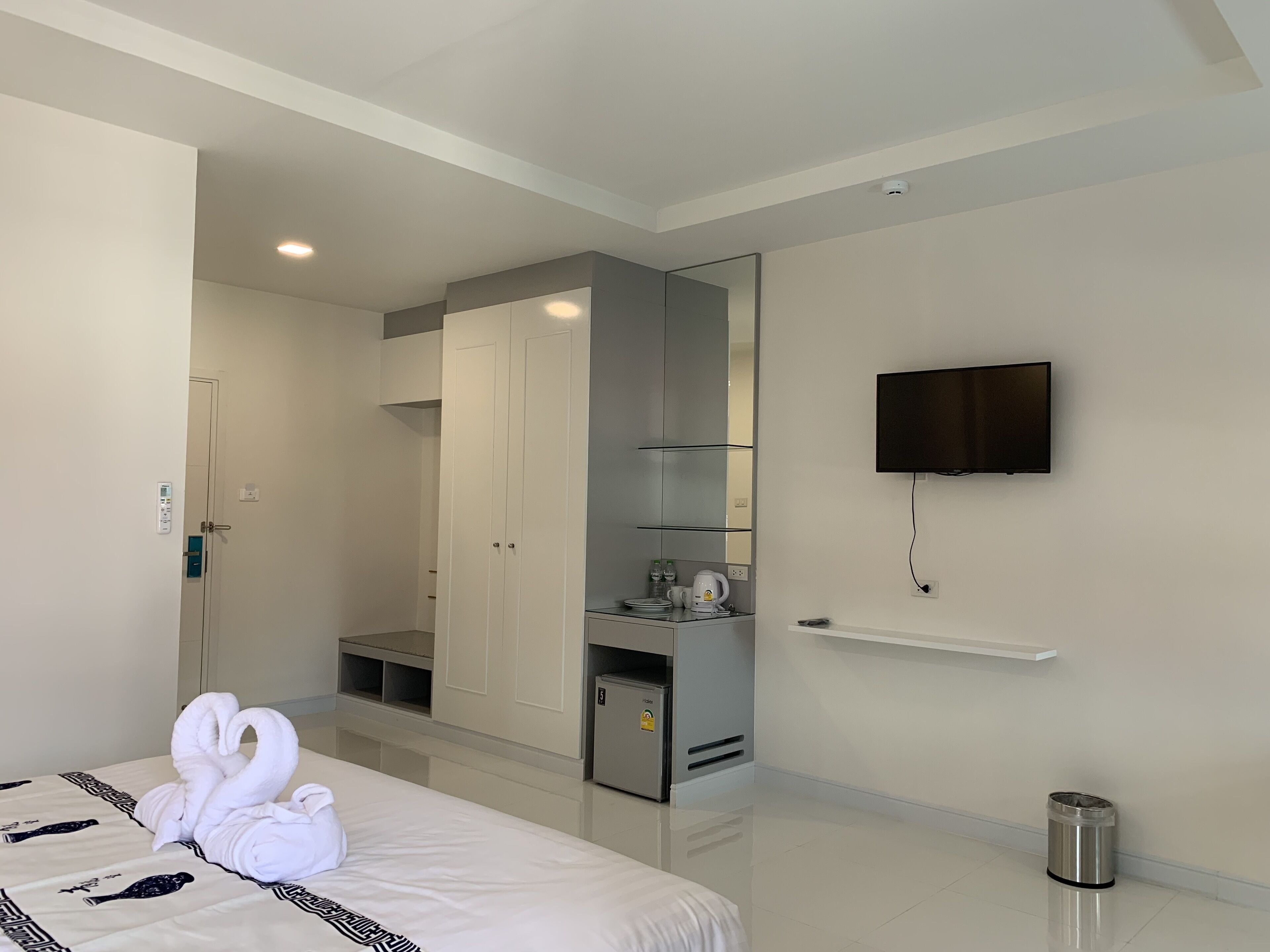 Habitación de hotel con cama, armario, televisor, kitchenette pequeña y un cesto de basura.