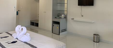 A hotel room with a bed, a wardrobe, a television, a small kitchenette, and a trash bin.
