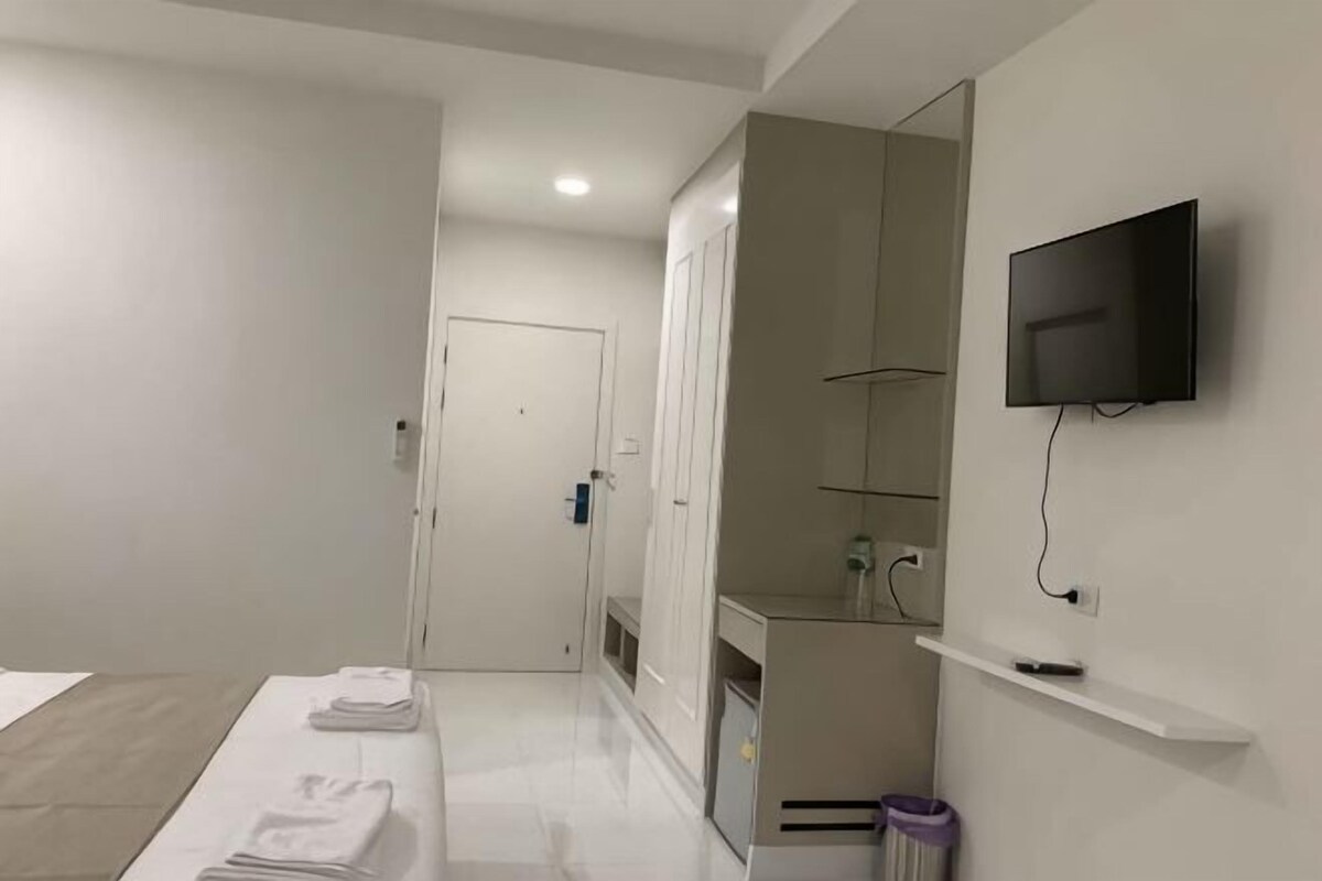 Una habitación de hotel moderna con una cama, un televisor montado en la pared, un espejo y un pequeño estante.