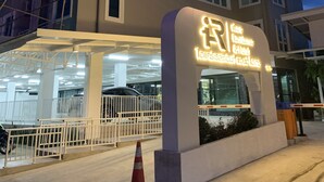Entrada de hotel con diseño moderno, destacándose un letrero iluminado, zona de estacionamiento techada y un edificio de varios pisos al fondo.