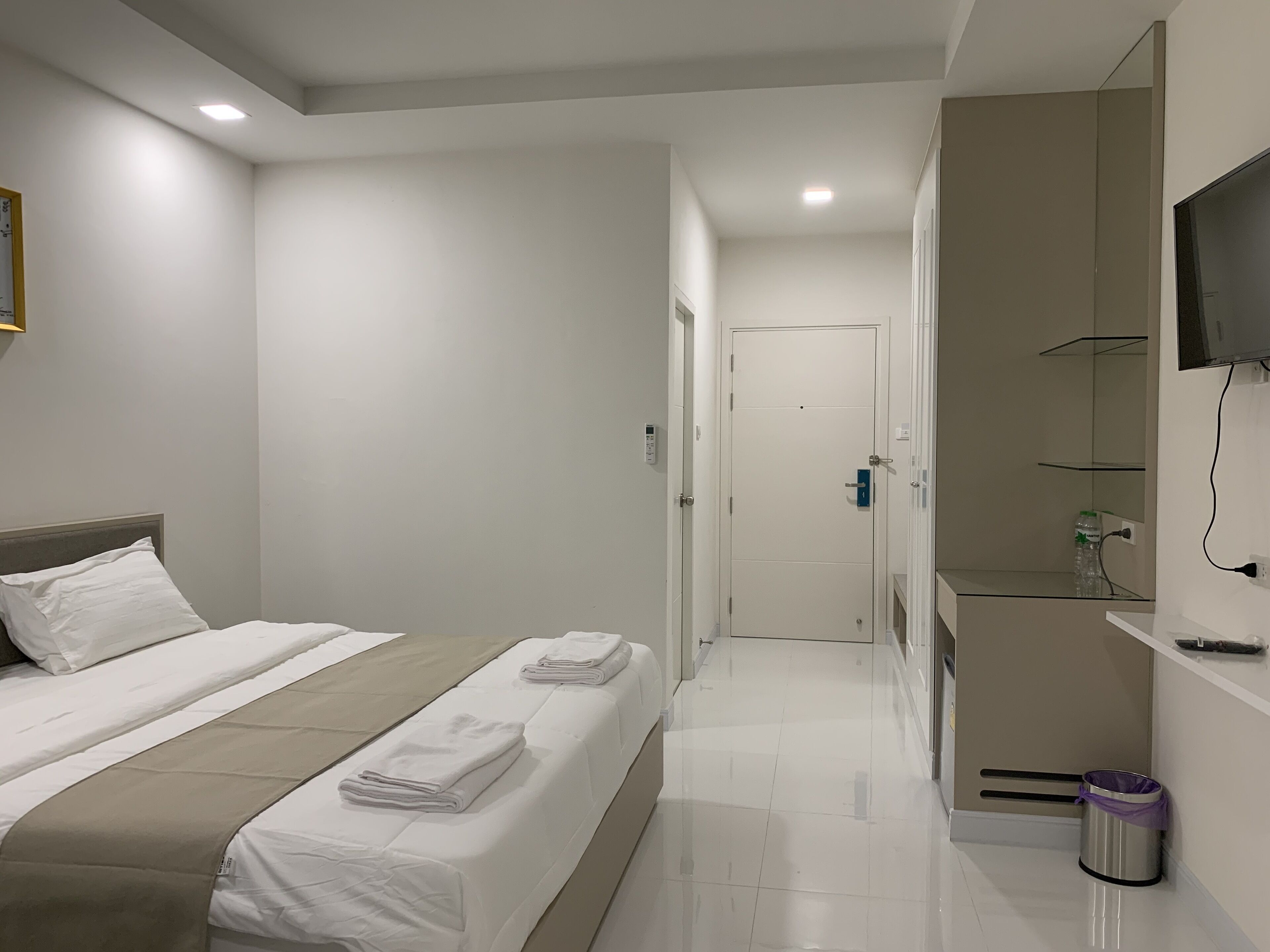 A hotel room with a bed, a bedside table, a TV mounted on the wall, and a bathroom with a shower and a toilet.