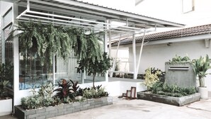 Un espacio exterior moderno con cerramiento de vidrio, plantas en macetas y una zona de jardineras de hormigón.