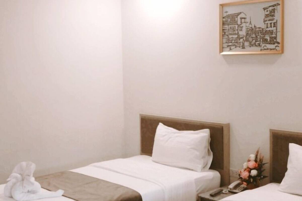 Habitación de hotel con dos camas individuales, una mesita de noche pequeña con un teléfono y un cuadro en la pared.