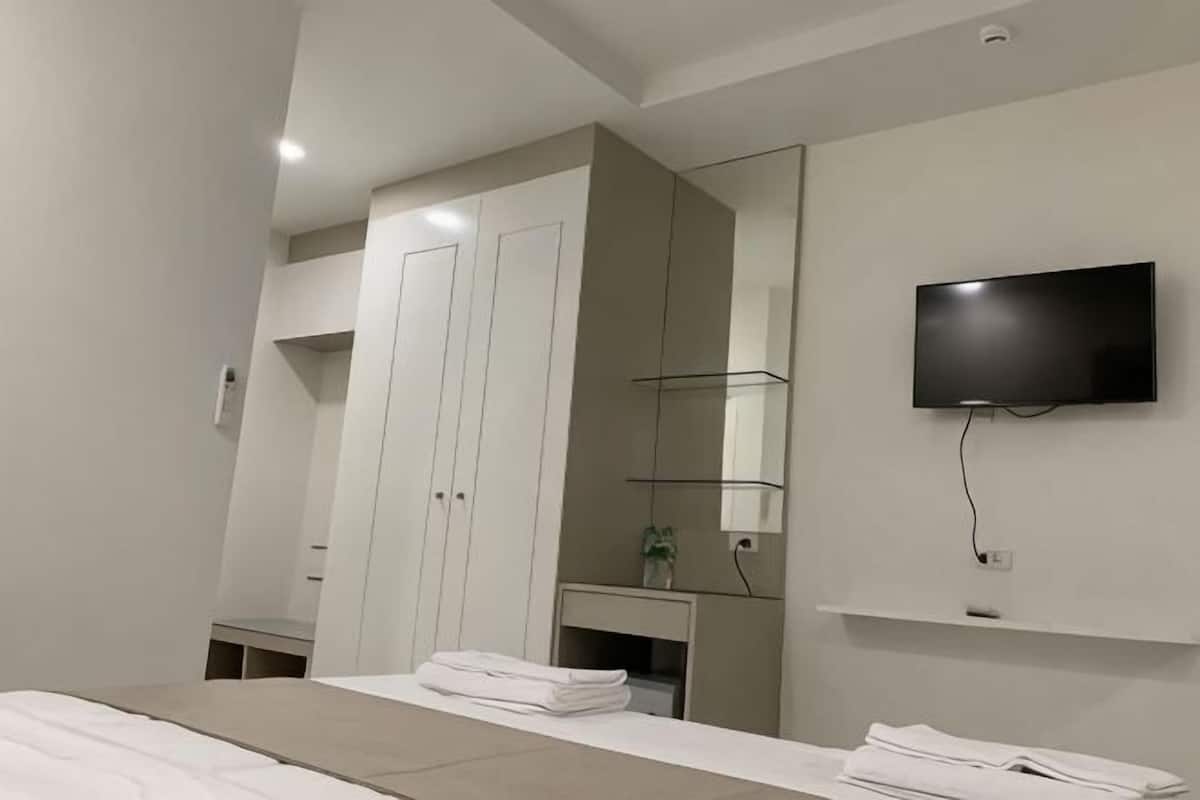 Una habitación de hotel moderna con una cama, un televisor montado en la pared, un armario y un pequeño escritorio con una planta.
