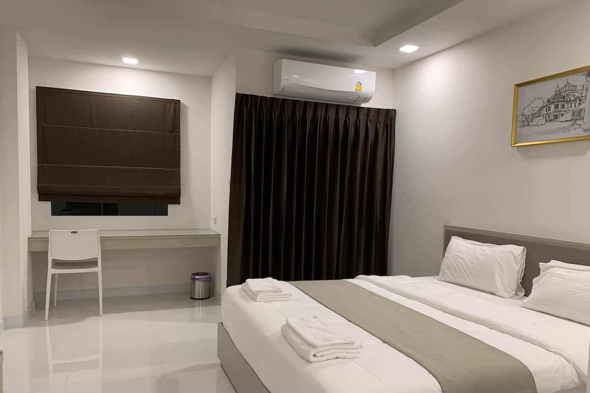Una habitación de hotel con cama, escritorio, silla, aire acondicionado, cortina e imagen enmarcada en la pared.
