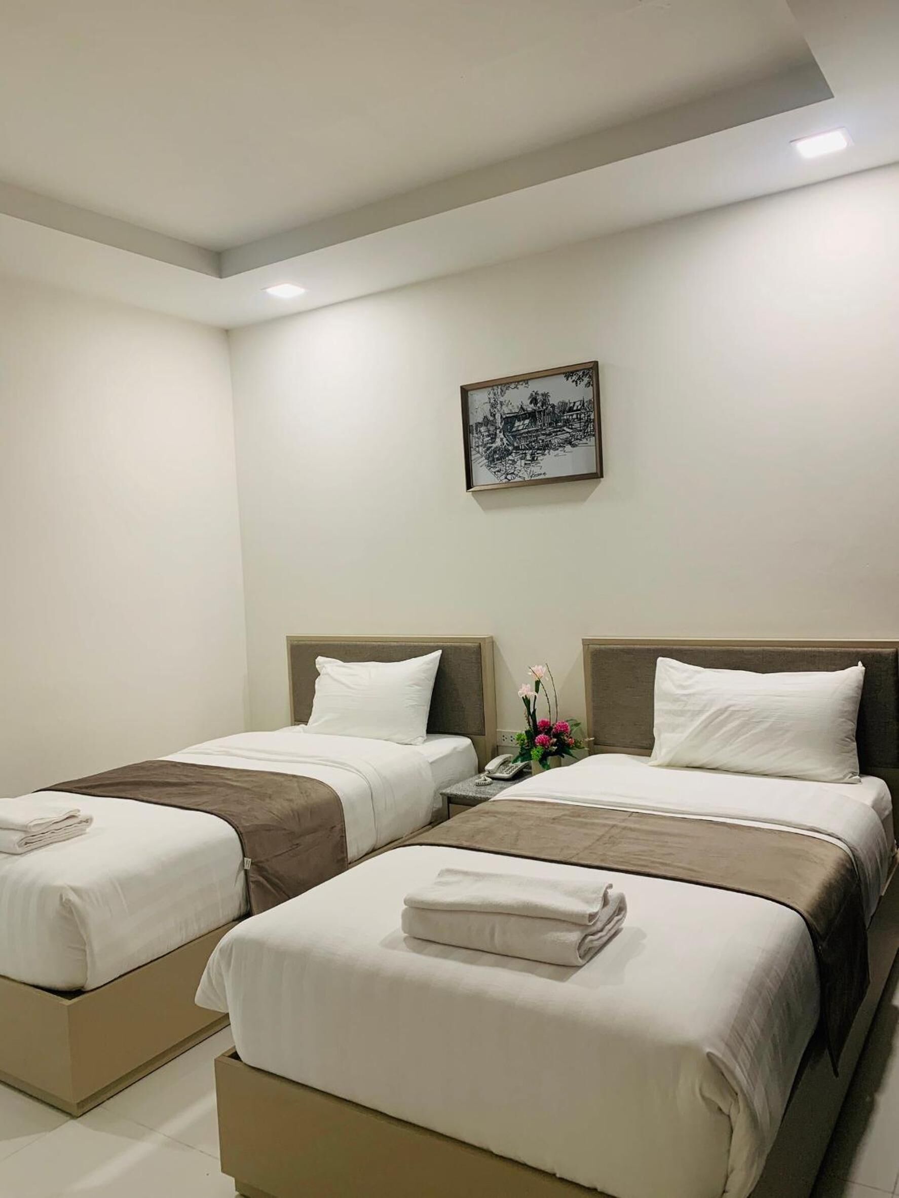 Une chambre d’hôtel avec deux lits, une table de chevet avec un téléphone et un tableau encadré au mur.