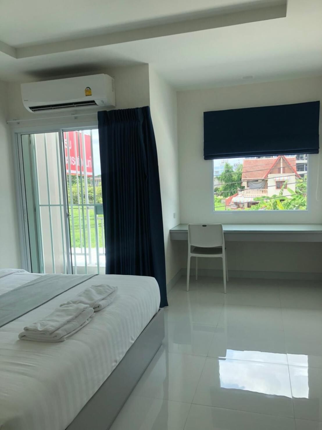 Une chambre d’hôtel avec un lit, un bureau et une fenêtre donnant sur une maison et de la verdure.