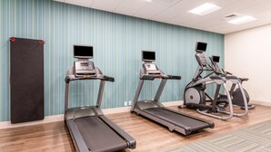 A fitness room with treadmills and elliptical machines, a black mat, and a patterned carpet.