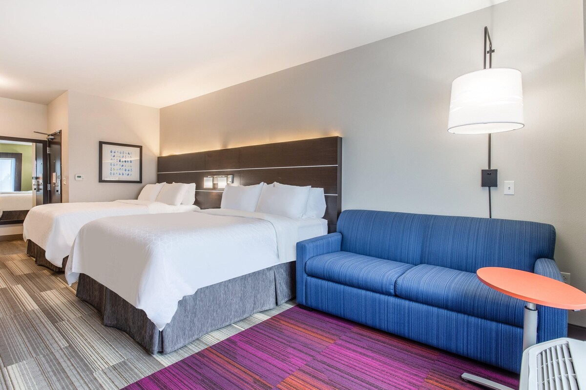Habitación de hotel con dos camas, un sofá, una mesita pequeña y una alfombra colorida.